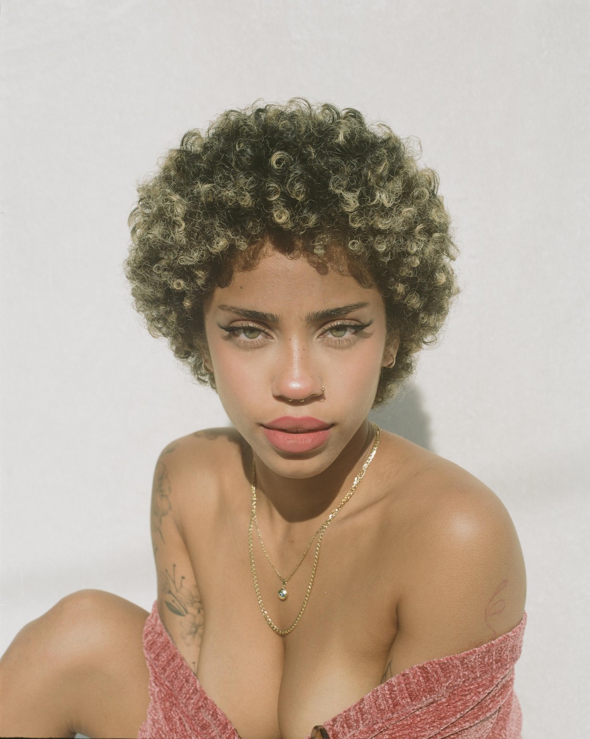 A woman with curly hair and a gold necklace looks directly at the viewer.