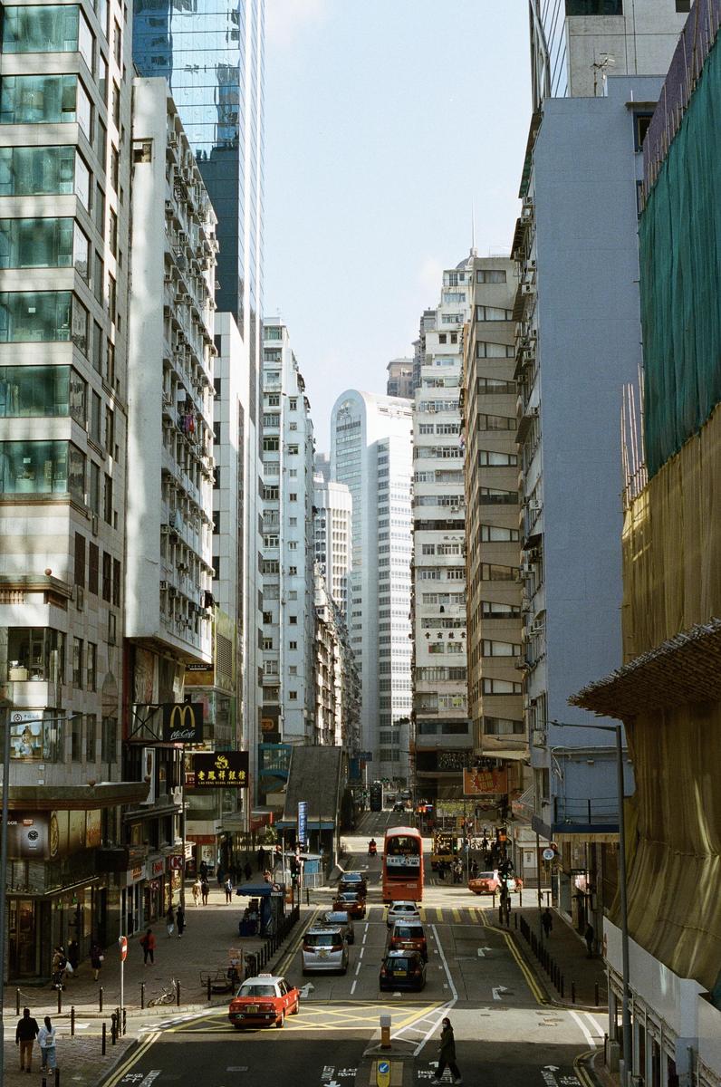 A busy street in Causeway Bay, Hong Kong, is lined with tall buildings and features cars and a double-decker bus.