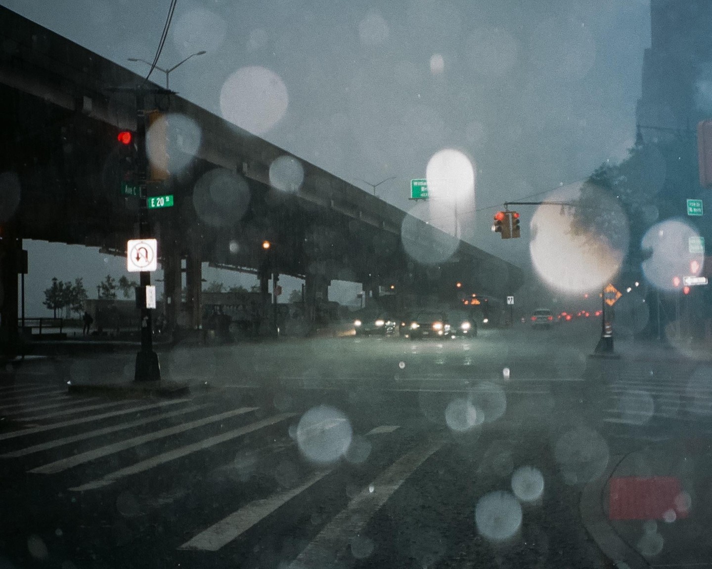 A street in New York is wet from rain, with cars driving under an overpass.