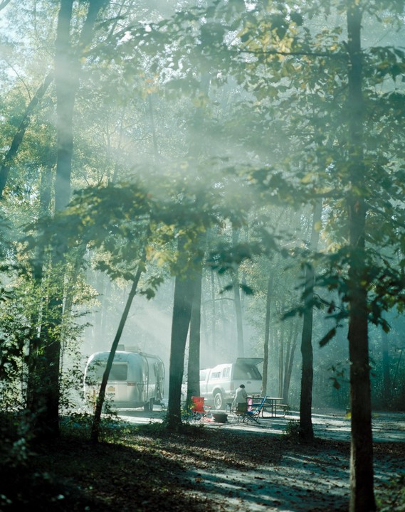 A person stands by a truck and a travel trailer in a hazy forest.