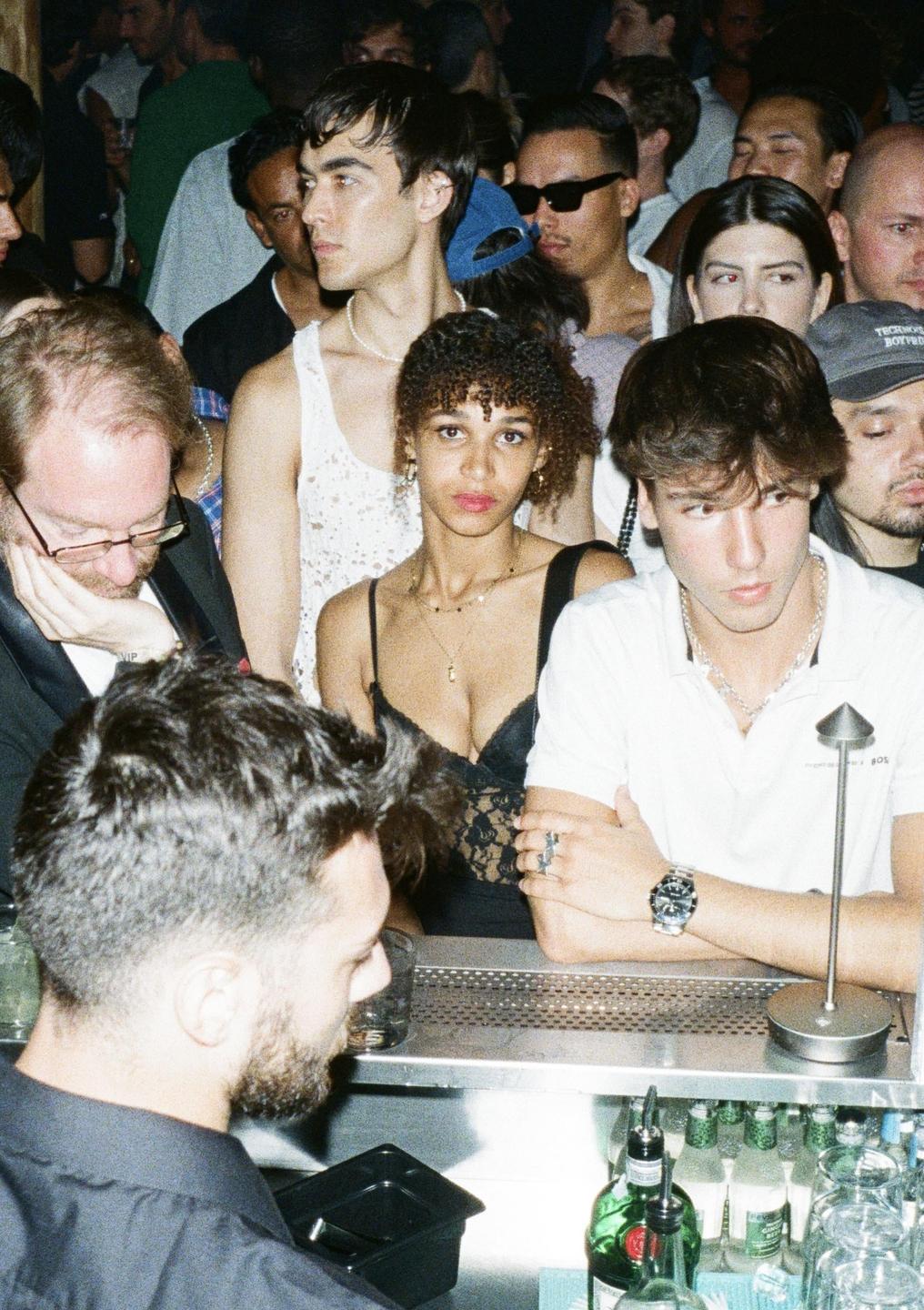 A group of people are gathered around a bar in a dimly lit club.
