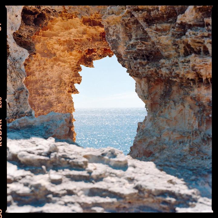 A natural rock arch frames a view of the sparkling ocean under a clear sky.