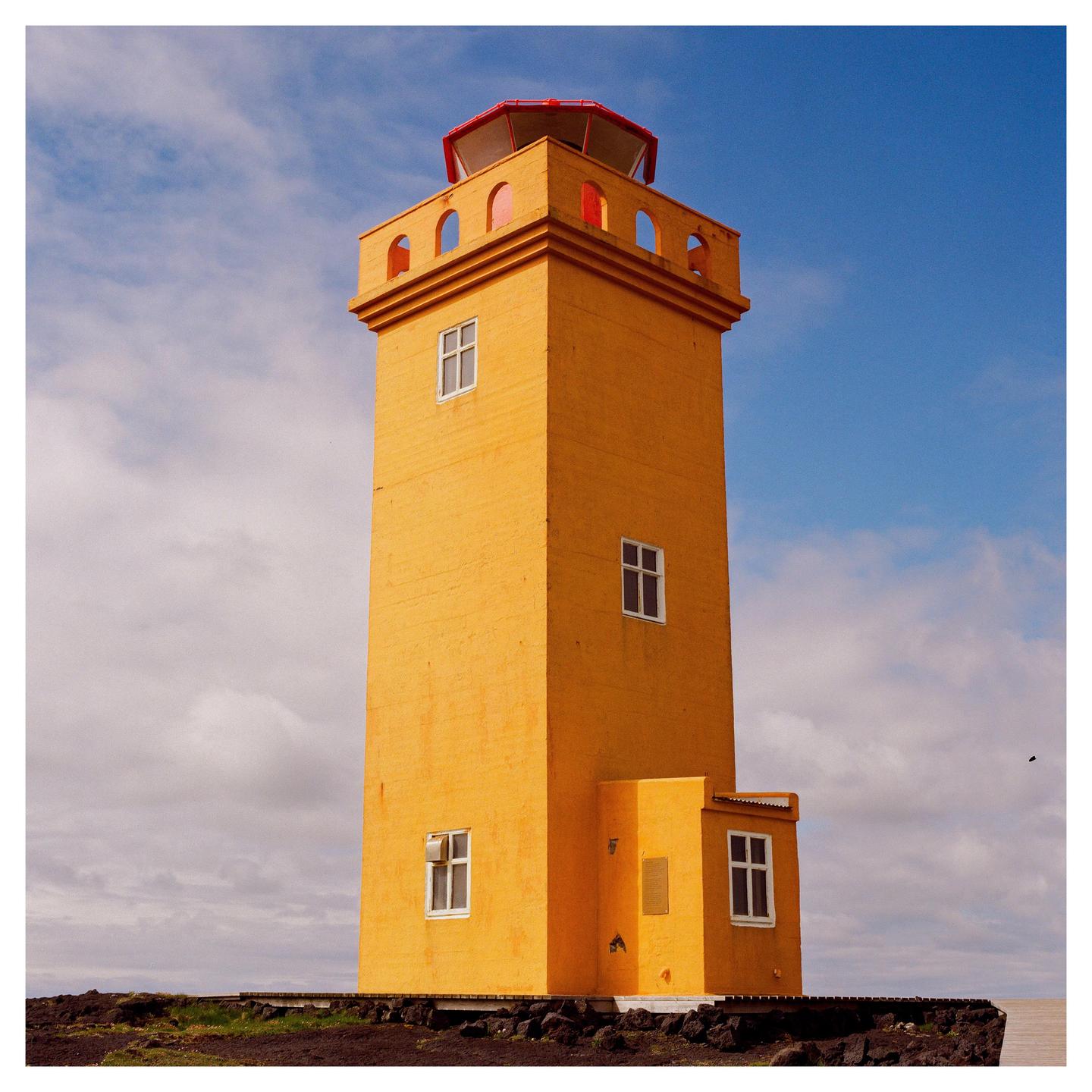 A tall, yellow lighthouse with a red top stands against a partly cloudy blue sky.