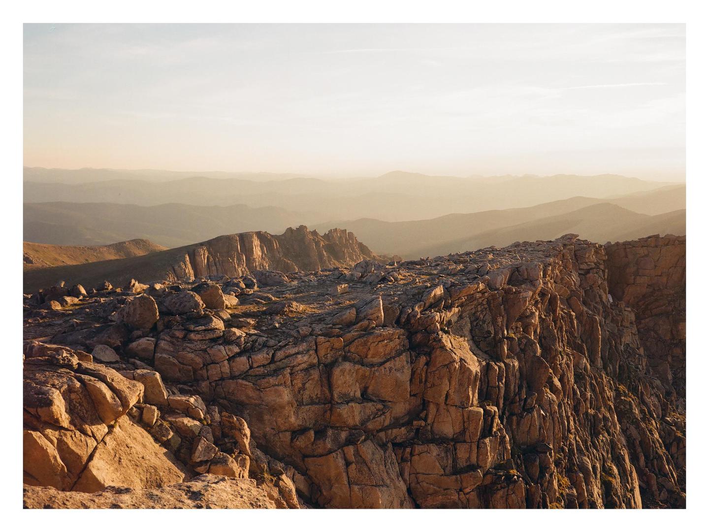 A rocky mountain ridge is illuminated by early morning light, with hazy mountains in the distance.