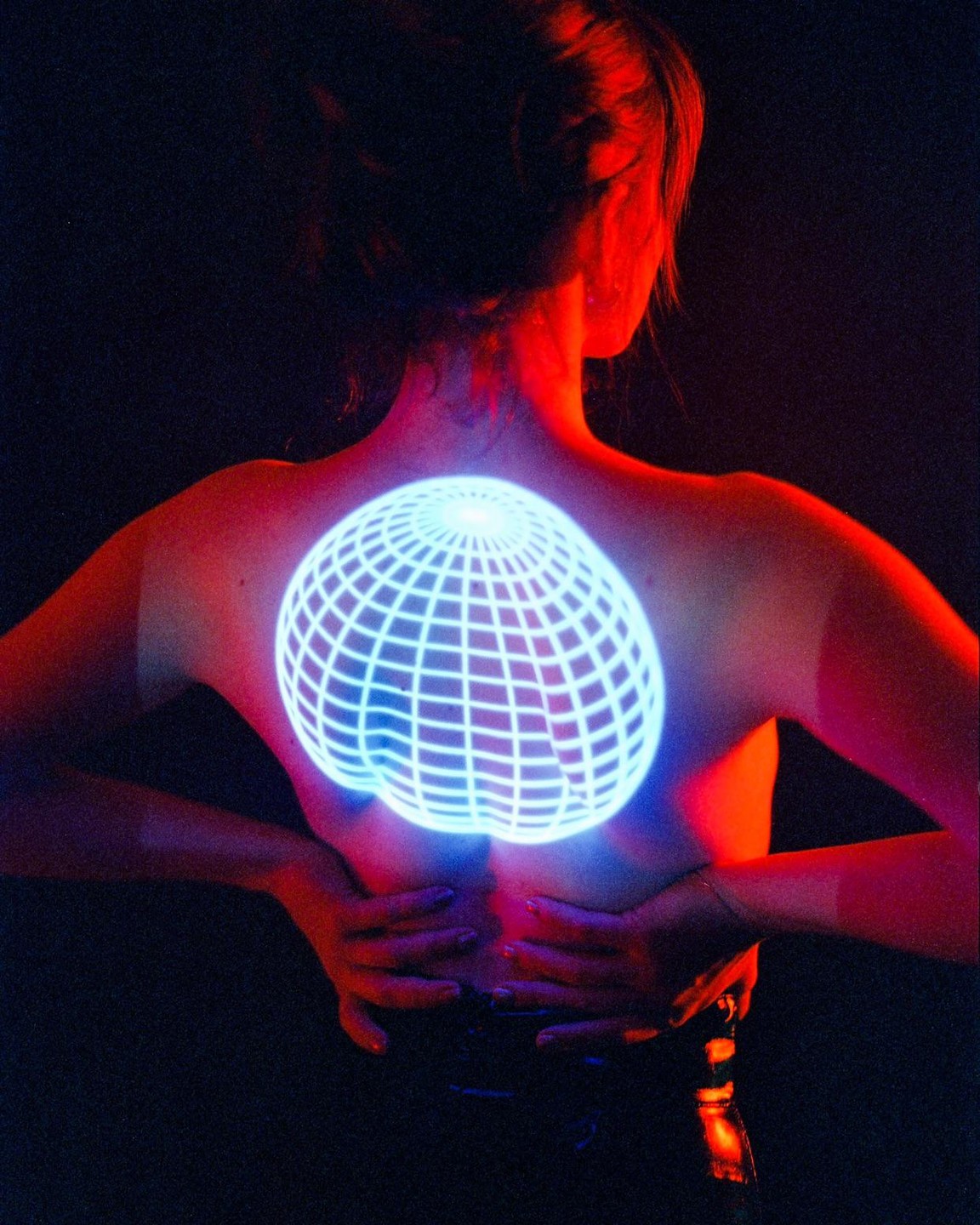 A woman's back is illuminated by a glowing blue grid pattern and red light.