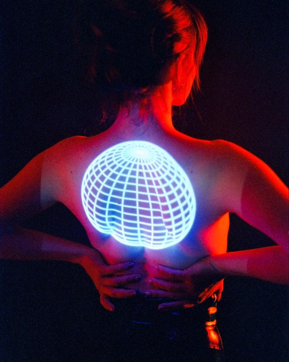 A woman's back is illuminated by a glowing blue grid pattern and red light.