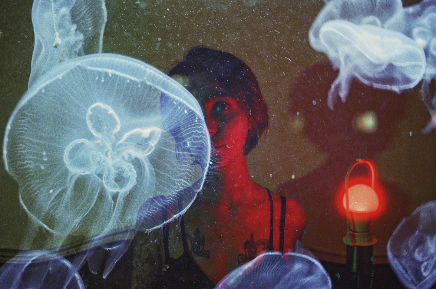 A woman with red skin is visible behind a jellyfish in a double exposure with a red lamp.