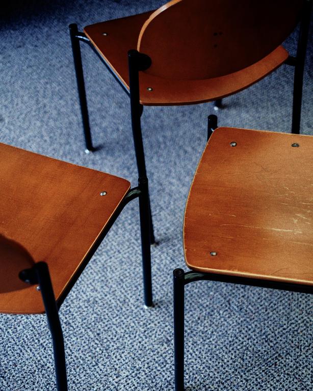 Three wooden chairs with black metal legs are arranged on a blue carpet.