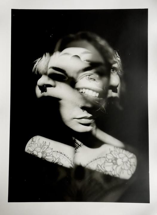 A woman's face is shown in multiple exposures with tattoos visible on her shoulders.