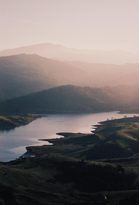 A hazy mountain landscape features a lake with a winding shoreline and rolling hills.