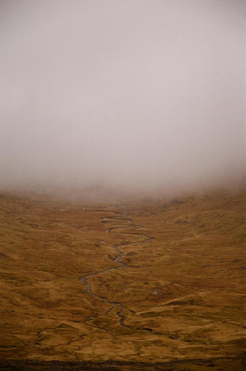 A winding river flows through a vast, misty landscape of brown and green vegetation.