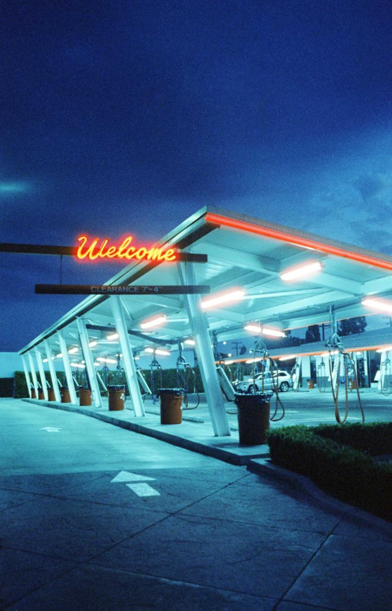 A neon "Welcome" sign illuminates a car wash at night.