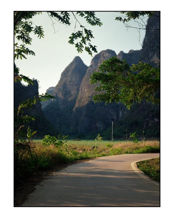 A winding road leads through a valley with towering karst mountains under a clear sky.