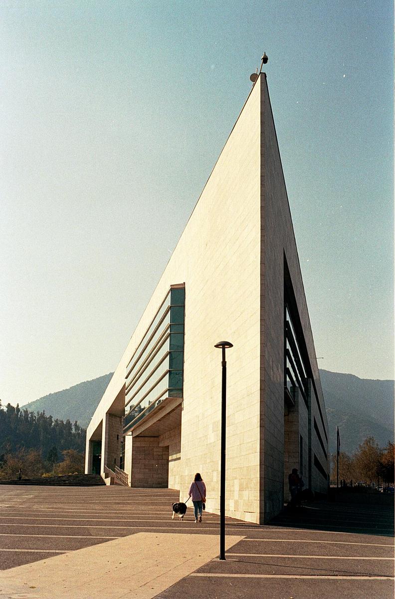 A woman walks a dog on a leash in front of a modern building with a mountain in the background.