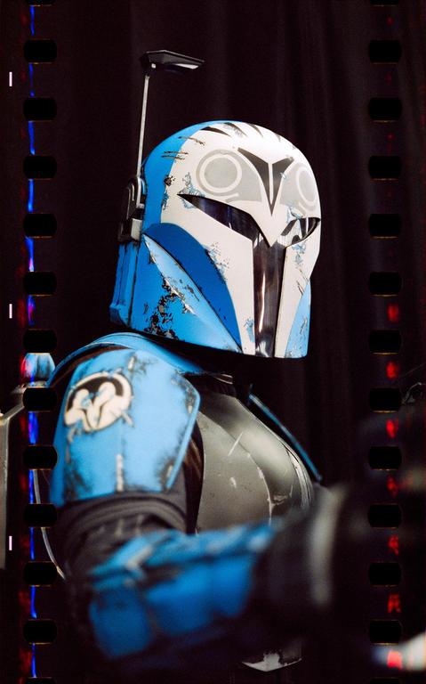 A person in a blue and white helmet and armor is visible in a close-up shot.