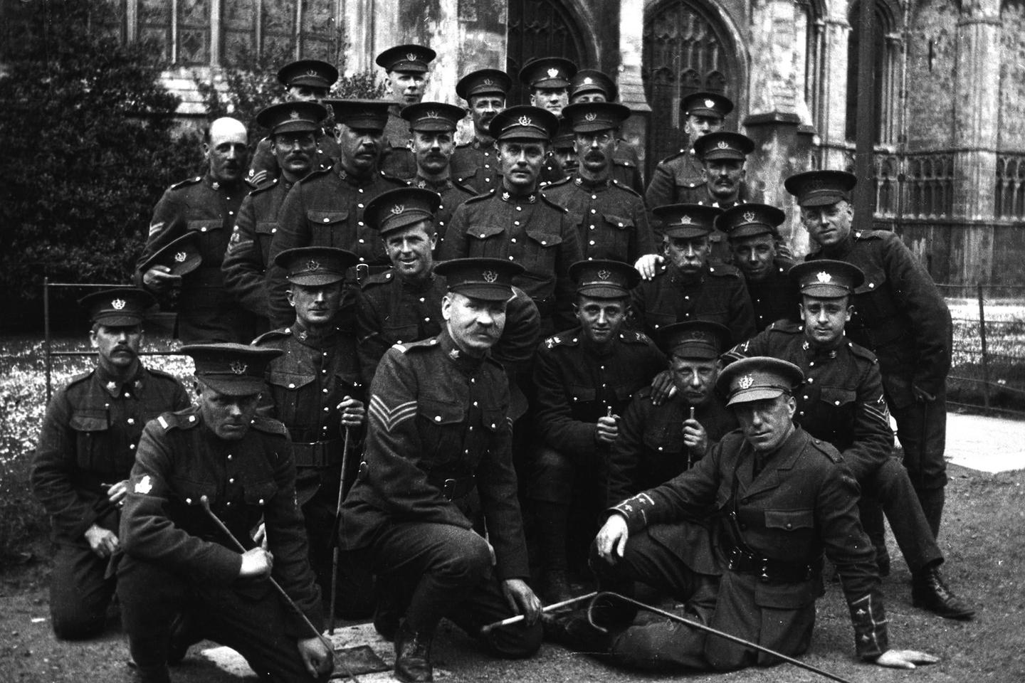 A group of men in military uniform pose for a portrait in front of a stone building.