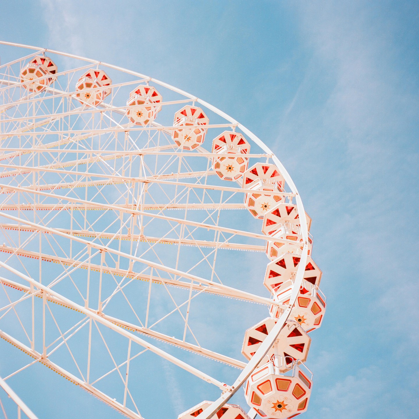 A white ferris wheel with red and gold gondolas stands against a clear blue sky.