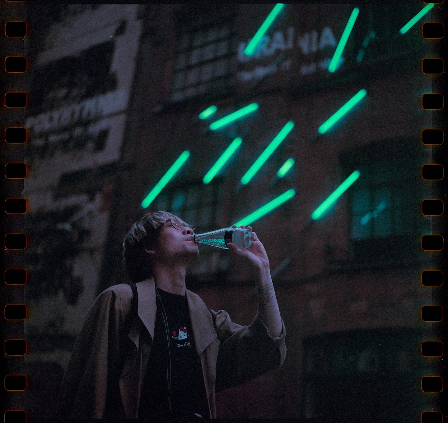 A man drinks from a bottle with neon lights in the background.