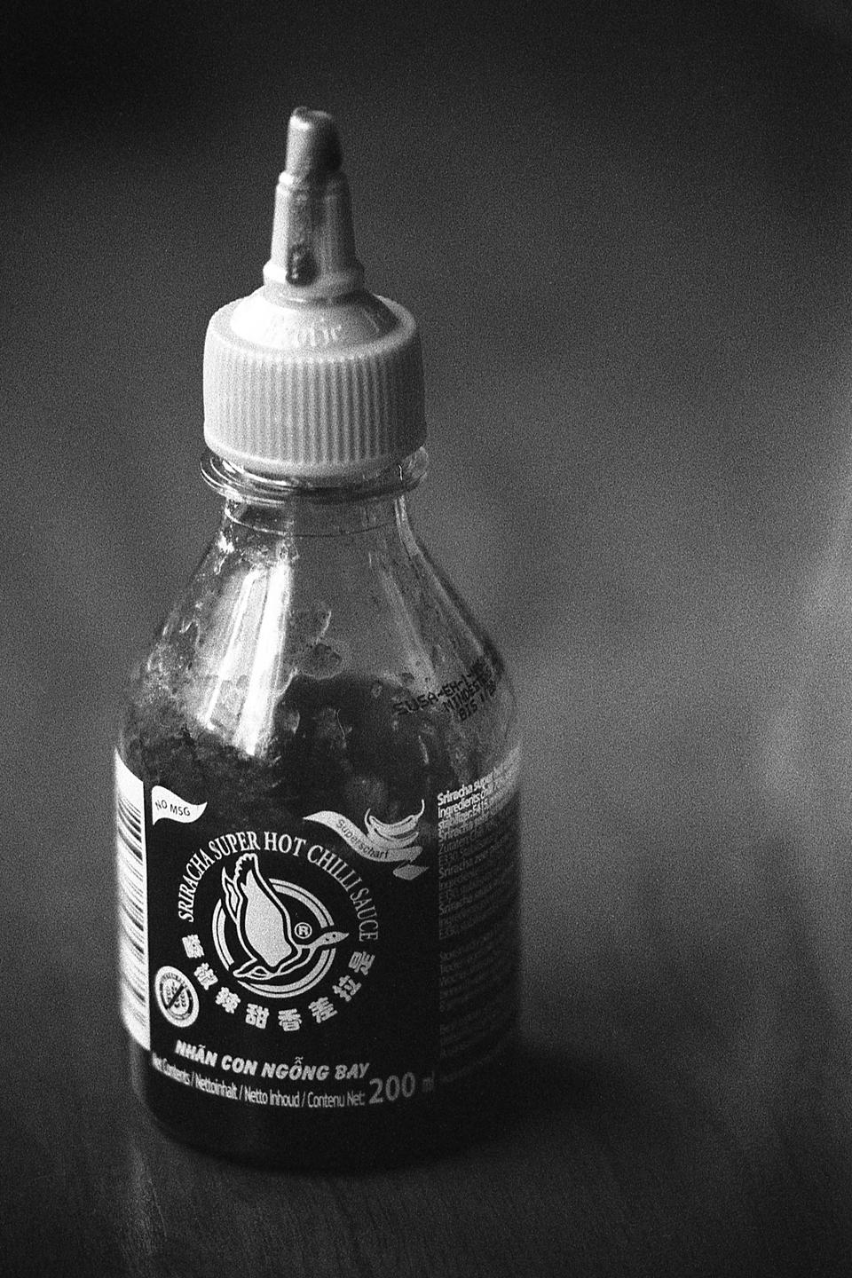 A bottle of sriracha super hot chili sauce stands on a surface.