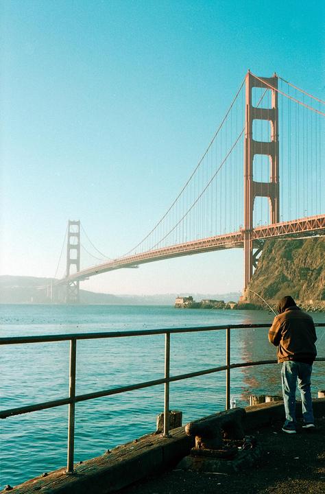 A man fishes from a pier with the Golden Gate Bridge in the background.