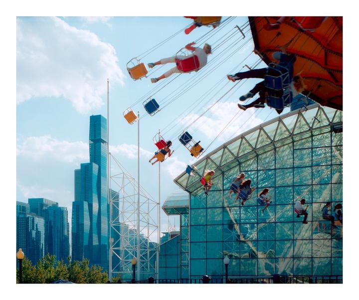 People ride a swing carousel at Navy Pier with a city skyline in the background.