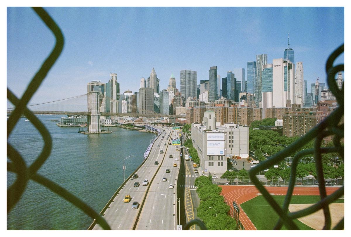 A city skyline with a bridge and a highway is seen through a chain-link fence.