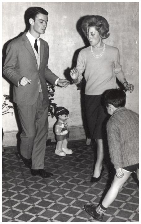A man, a woman, and a child are dancing on a tiled floor next to a Pinocchio doll.