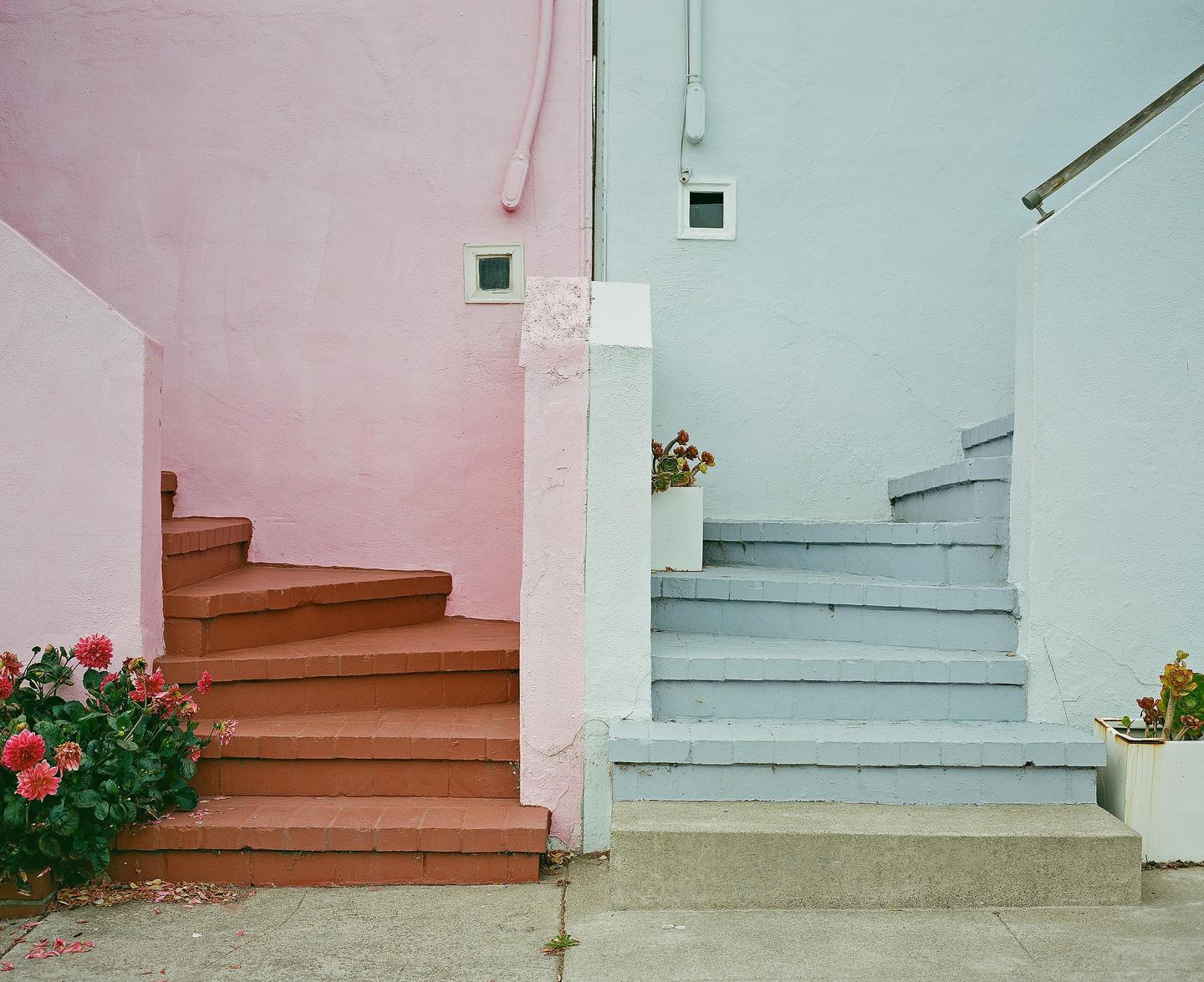 Two sets of outdoor stairs, one pink and one blue, lead up to unseen entrances.