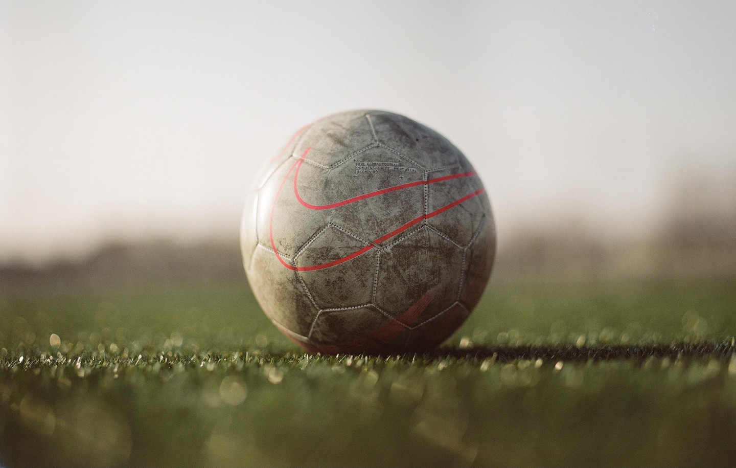 A worn soccer ball with red markings rests on green grass.