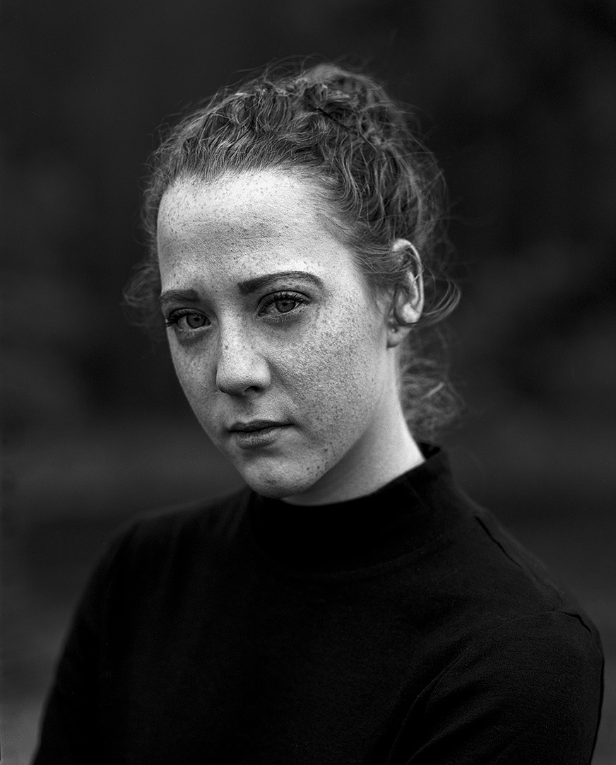 A woman with freckles and curly hair looks directly at the viewer.