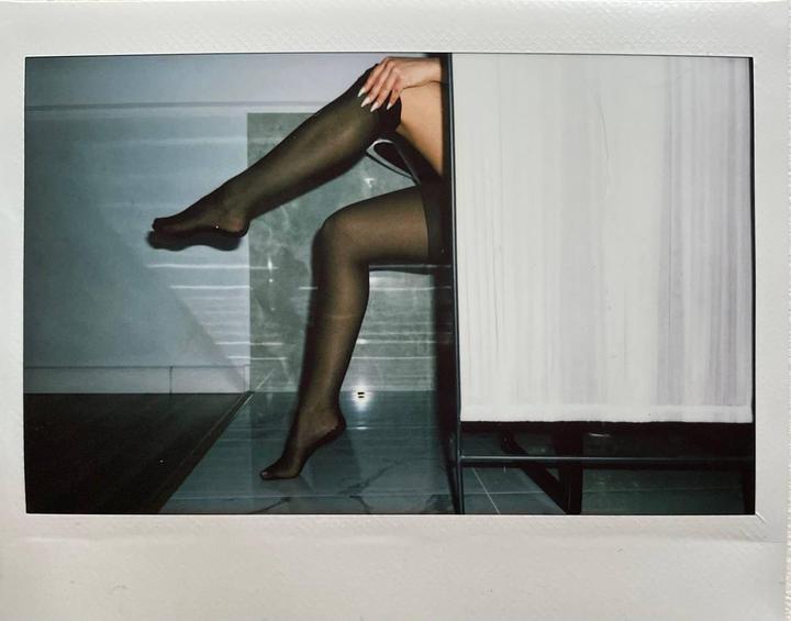 A woman's legs in sheer stockings are visible next to a white curtain.