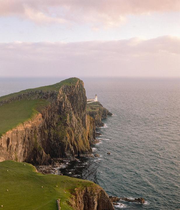 A lighthouse stands on a cliff overlooking the ocean under a cloudy sky.