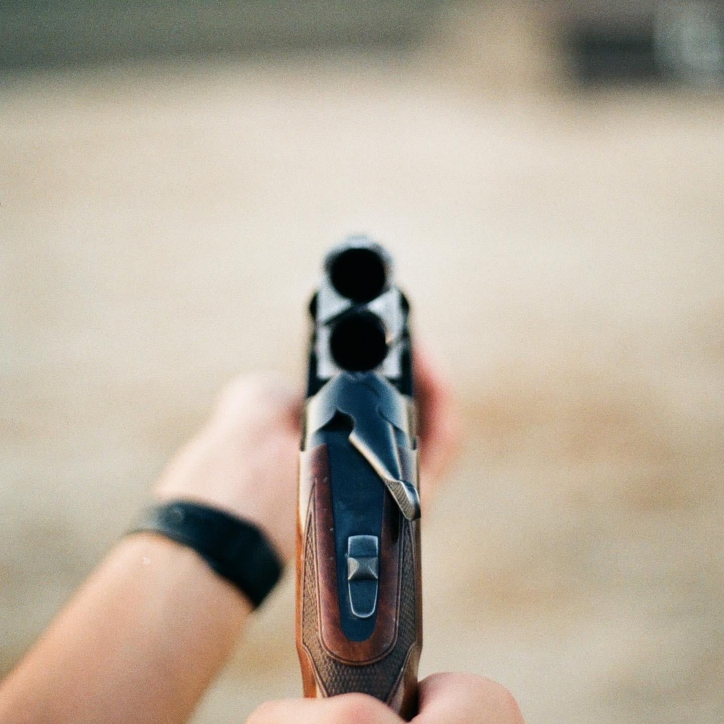A person holds a shotgun pointed directly at the viewer.