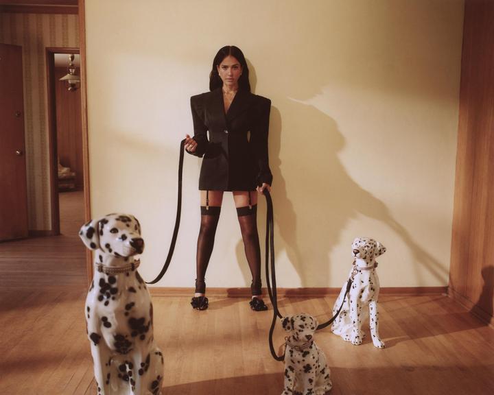 A woman in a blazer and stockings holds leashes attached to three dalmatian statues.