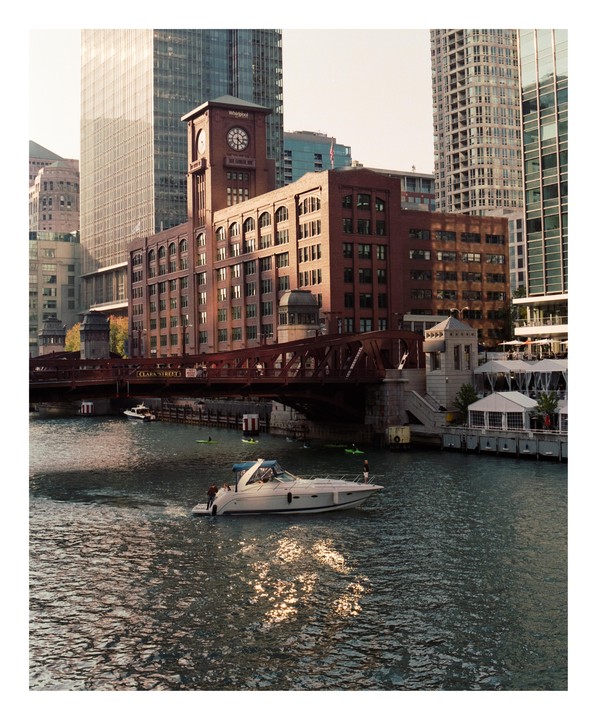 A boat travels on a river in a city with tall buildings and a bridge.