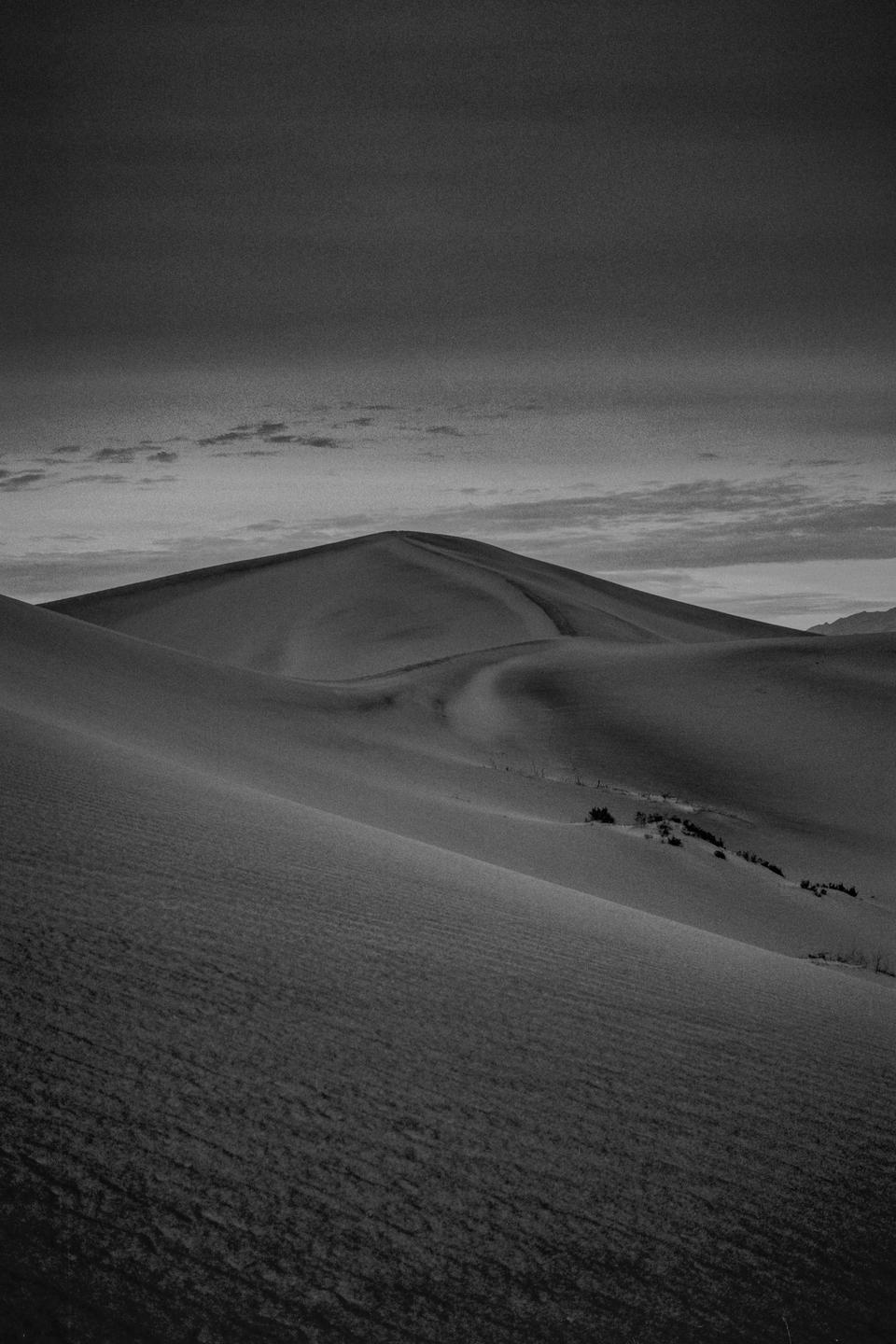 A black and white landscape shows sand dunes under a cloudy sky.