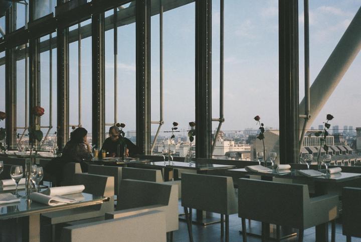 A couple sits at a table in a restaurant with large windows overlooking a city.