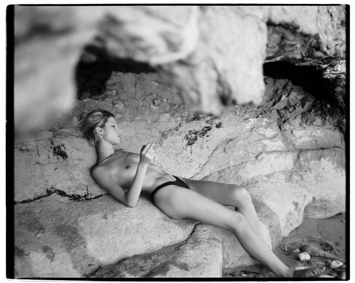 A woman in a bikini bottom is lying on a rock.