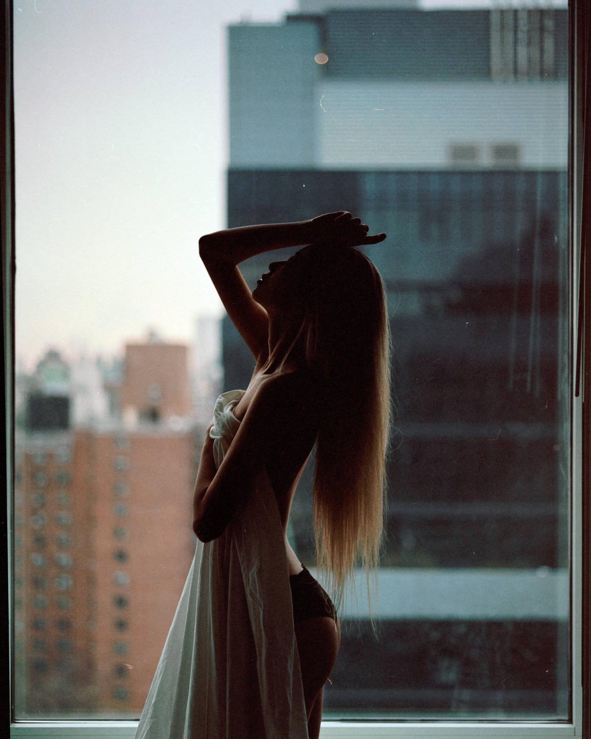 A woman stands in front of a window, silhouetted against a city skyline.