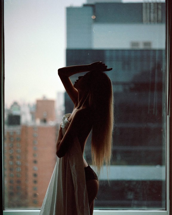 A woman stands in front of a window, silhouetted against a city skyline.