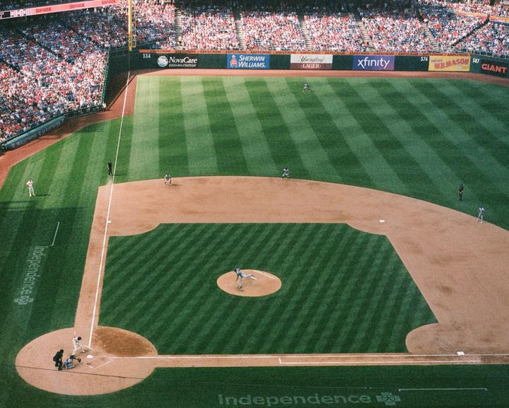 An aerial view shows a baseball game in progress with players on the field and spectators in the stands.