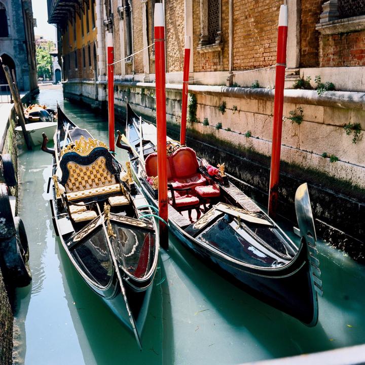 Two gondolas are moored in a canal next to a brick building.