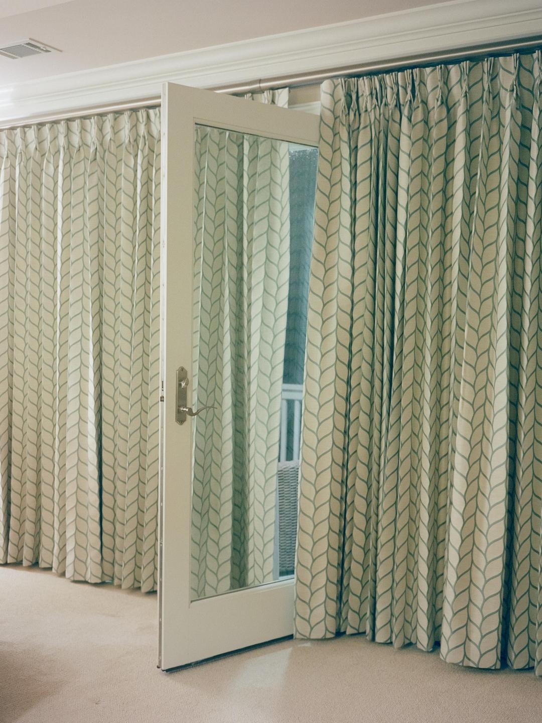 A white door with a glass panel is slightly ajar, revealing a reflection of patterned curtains and a glimpse of an outdoor setting.