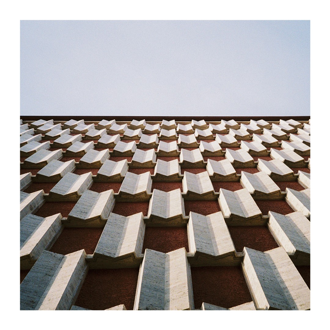 A building facade features a repeating pattern of geometric shapes against a clear sky.