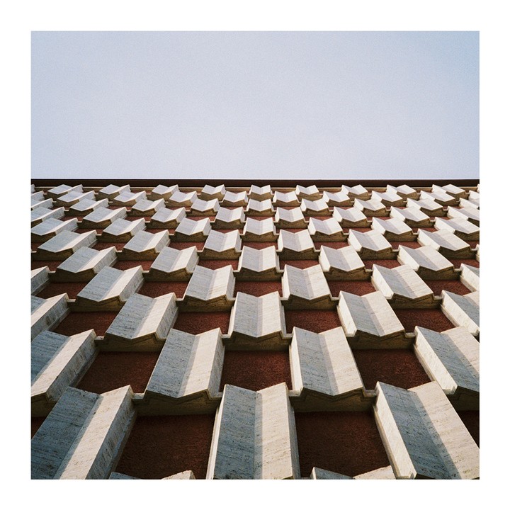 A building facade features a repeating pattern of geometric shapes against a clear sky.
