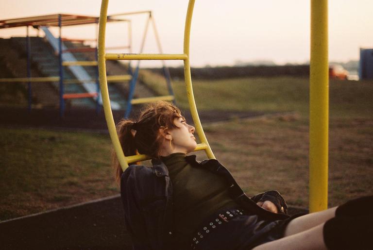 A young woman with a ponytail is sitting on a yellow playground structure, looking up and to the right.