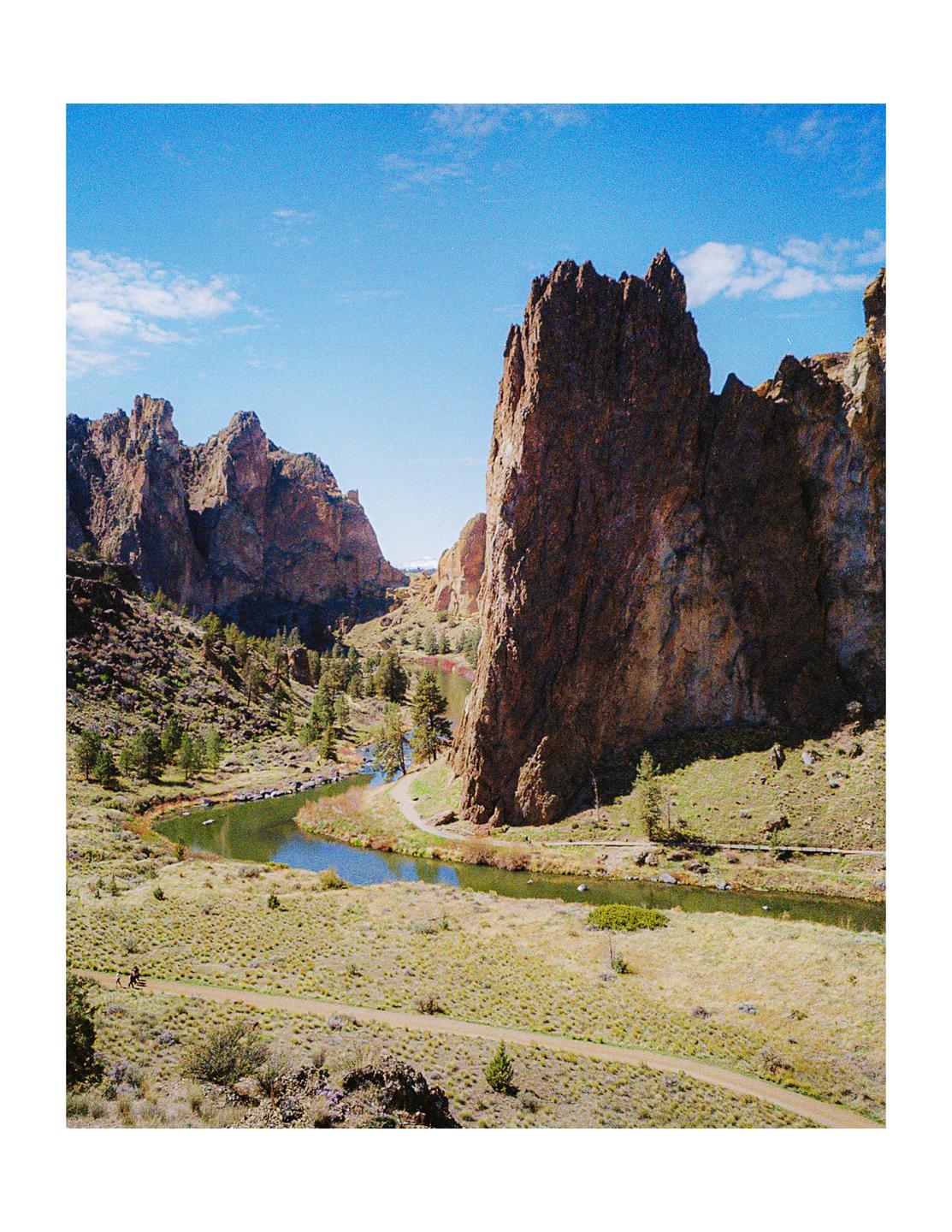 A winding river flows through a valley surrounded by towering rock formations under a bright blue sky.