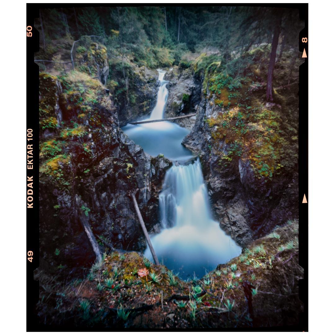 Two waterfalls cascade into pools surrounded by rocky, moss-covered cliffs and forest.
