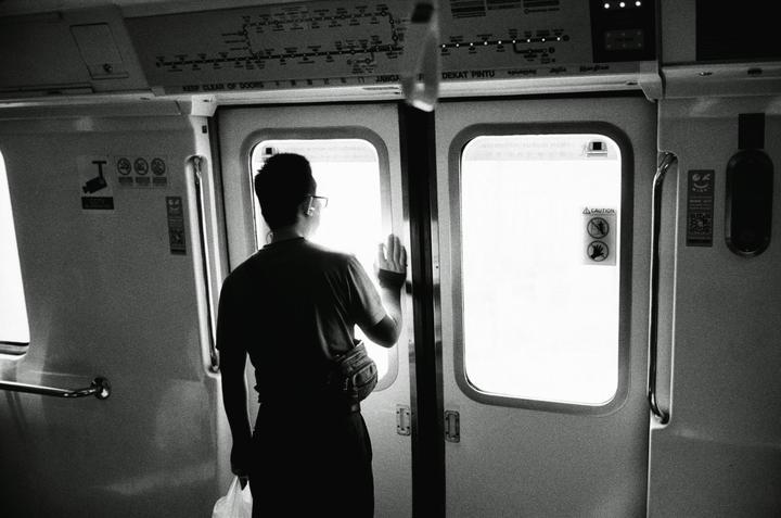 A man stands with his back to the camera, looking out a brightly lit train door.