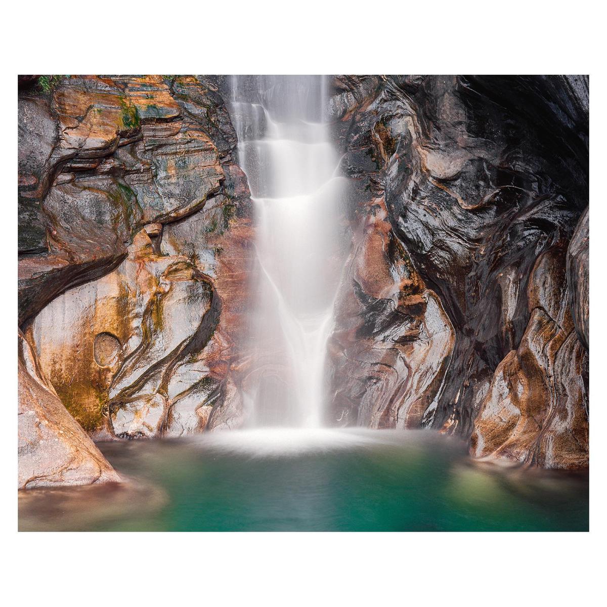 A waterfall cascades into a pool of turquoise water surrounded by colorful rock formations.